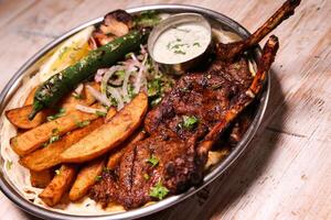 Riyash lamb chop with salad, wedges, lemon and dip served in dish isolated on background top view of arabic food photo