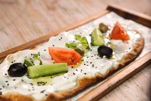 Labneh pizza bread with olives, tomato and cucumber served in wooden board isolated on background top view of Arabic Manaqeesh photo