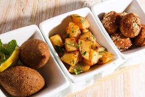 hot mezza with Kebbeh, kibbe, kebbah, kibbeh,Batata Harra or lebanese spicy potatoes and falafel served in dish isolated on background top view of hot mezza photo