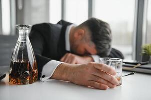 cerca arriba de estresado empresario participación un vaso de whisky él dormido y datos gráficos, negocios documento a oficina escritorio. alcohol adiccion y borracho empresario concepto foto