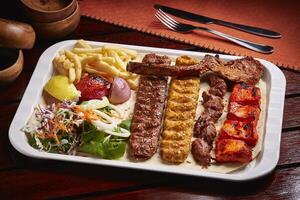 Spicy bbq Mixed Grills platter with tikka boti kababs, fries, salad served in dish isolated on table side view of middle east food photo