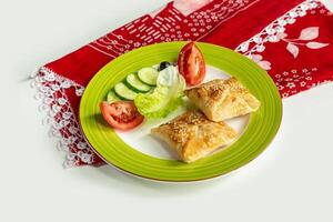 Turkish Peynirli Borek with cheese and salad in a dish isolated on colorful table cloth top view on grey background photo