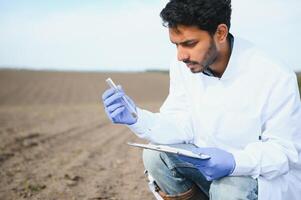 Soil Test. Indian Agronomist putting soil with garden shovel in soil sample bag outdoor. Environmental research photo