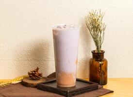 Iced Beidao purple taro fresh milk served in disposable glass isolated on wooden board side view of taiwanese ice drink photo