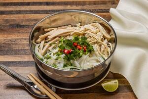 Shredded Chicken and Sausage Pho topping with noodles, spring onion, red chilli, coriander and chopsticks served in bowl isolated on wooden table top view of hong kong fast food photo