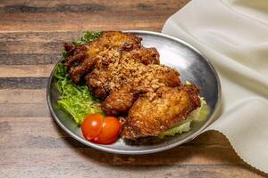 Gaarlic Butter Chicken Wings with lettuce leaf and tomato served in dish isolated on wooden table top view of hong kong fast food photo