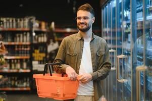 hombre con un barba compra un cerveza en el alcohol Departamento de un supermercado . hermoso hombre elige un cerveza botella en el Tienda y comunica en un smartphone.compras en un supermercado foto