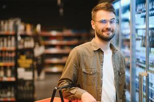 Man with a beard buys a beer in the alcohol department of a supermarket . Handsome man chooses a beer bottle in the store and communicates on a smartphone.Shopping in a supermarket photo