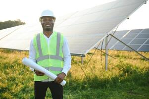 Close up portrait of young african american engineer worker in hardhat holding solar plan. Green electricity future concept. photo