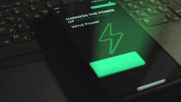 Harness the power of green energy. Wind Power. Inscription on smartphone screen. Graphic presentation with flickering Energy symbol on black background. Power and energy concept. Light rays video