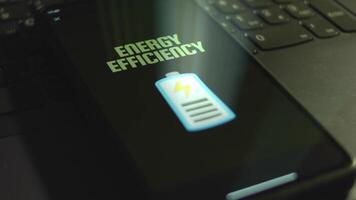 Energy Efficiency inscription on smartphone screen. Graphic presentation of battery, charge symbol on black background. Light rays. Power and Energy concept video