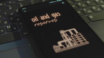 Oil and Gas Reserves inscription on smartphone screen with black background. Graphic presentation with oil production plant silhouette. Oil and gas concept video