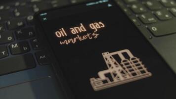 olie en gas- markten opschrift Aan smartphone scherm met zwart achtergrond. grafisch presentatie met natuurlijk gas- productie fabriek symbool. olie en gas- concept video
