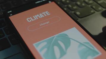 Climate change inscription on orange background on smartphone screen. Drawn image with green leaves. Environment concept. Male hand flapping fingers cheerfully video