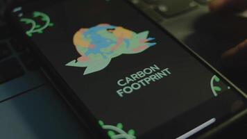 Carbon footprint inscription on smartphone screen. Drawn image of Planet Earth hugged by two people. Environment concept. Male hand flapping fingers cheerfully video