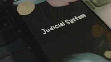 Judicial System inscription on smartphone screen. Graphic presentation on black background with bokeh lights. Light rays. Legal concept video