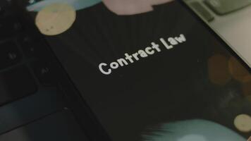 Contract Law inscription on smartphone screen. Graphic presentation on black background with bokeh lights. Light rays. Legal concept video