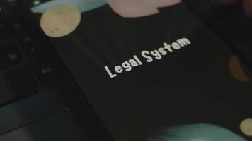 Legal System inscription on smartphone screen. Graphic presentation on black background with bokeh lights. Light rays. Legal concept video