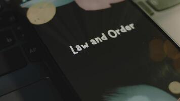 Law and Order inscription on smartphone screen. Graphic presentation on black background with bokeh lights. Light rays. Legal concept video