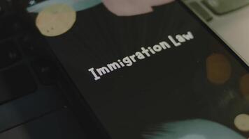 Immigration Law inscription on smartphone screen. Graphic presentation on black background with bokeh lights flickering . Light rays. Legal concept video