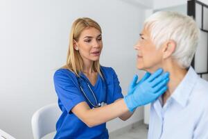 endocrinólogo examinando garganta de mayor mujer en clínica. mujer con tiroides glándula prueba . endocrinología, hormonas y tratamiento. inflamación de el dolorido garganta foto