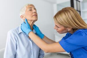 Endocrinologist examining throat of senior woman in clinic. Women with thyroid gland test . Endocrinology, hormones and treatment. Inflammation of the sore throat photo