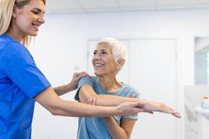 Photo of physiotherapist working with a senior female patient in her office during the day. Physiotherapist helping female patient during muscle rehabilitation physiotherapy