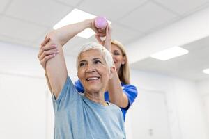 Medical, training and physiotherapy with dumbbell and old woman with nurse for rehabilitation, support and retirement. Healthcare, help and physical therapy with patient and doctor in nursing home photo