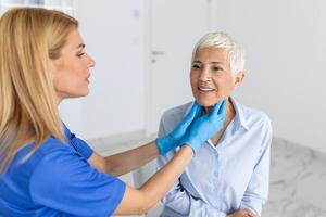 Endocrinologist examining throat of senior woman in clinic. Women with thyroid gland test . Endocrinology, hormones and treatment. Inflammation of the sore throat photo