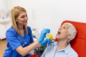 Doctor taking throat swab test from senior female patient. Medical worker is in protective workwear. They are at hospital during epidemic. photo