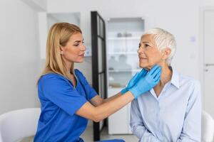 endocrinólogo examinando garganta de mayor mujer en clínica. mujer con tiroides glándula prueba . endocrinología, hormonas y tratamiento. inflamación de el dolorido garganta foto