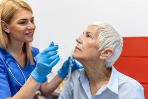 hembra paciente siendo probado para covid-19 con un nasal torunda, por un salud profesional protegido con guantes y ppe traje. rápido antígeno prueba durante coronavirus pandemia. foto