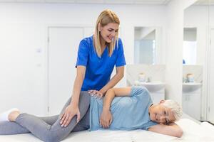 Professional chiropractor or physiotherapist helps to heal a senior woman's back. Doctor fixes the patient lying on a couch of a modern rehabilitation clinic Concept of physical rehabilitation. photo