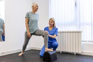 mayor paciente a el fisioterapia haciendo físico ejercicios con su terapeuta, haciendo pierna fisioterapia para mayor mujer, a tratar osteoartritis y nervio dolor en el pierna. foto