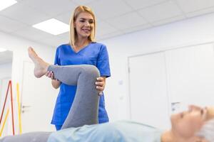 fisioterapeuta trabajando con paciente en clínica, de cerca. un moderno rehabilitación fisioterapia trabajador con mayor cliente, físico terapeuta extensión paciente rodilla foto