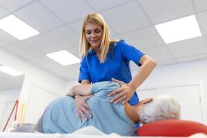 Doctor or physiotherapist helps to heal a senior woman's back. and give advice within the rehabilitation center. Concept of physical rehabilitation. photo