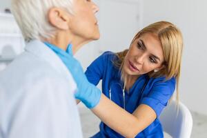 simpático mujer médico vistiendo guantes comprobación dolorido garganta o tiroides glándulas, conmovedor cuello de mayor hembra paciente visitando clínica oficina. tiroides cáncer prevención concepto foto