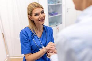 Doctor giving hope. Close up shot of young female physician leaning forward to smiling elderly lady patient holding her hand in palms. Woman caretaker in white coat supporting encouraging old person photo