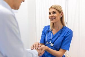 Doctor giving hope. Close up shot of young female physician leaning forward to smiling elderly lady patient holding her hand in palms. Woman caretaker in white coat supporting encouraging old person photo