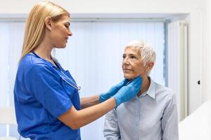 endocrinólogo examinando garganta de mayor mujer en clínica. mujer con tiroides glándula prueba . endocrinología, hormonas y tratamiento. inflamación de el dolorido garganta foto