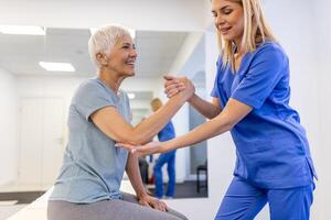 médico ortopédico enseñando mayor mujer a hacer osteoporosis tratamiento ejercicio en moderno clínica. fisioterapeuta Ayudar hembra paciente durante músculo rehabilitación fisioterapia foto