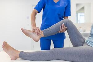 close up of female physiotherapist is helping senior elder woman stretching her hamstring and doing thigh or leg rehabilitation in exercise room - she is lying on massage bed photo