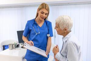 Young female doctor consulting senior old patient filling form at consultation. Professional physician uniform talking to mature woman signing medical paper at appointment visit in clinic. photo