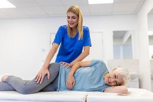 Professional chiropractor or physiotherapist helps to heal a senior woman's back. Doctor fixes the patient lying on a couch of a modern rehabilitation clinic Concept of physical rehabilitation. photo