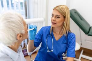 mayor paciente apertura su boca para el médico a Mira en su garganta. hembra médico examinando dolorido garganta de paciente en clínica. otorrinolaringólogo examina dolorido garganta de paciente. foto