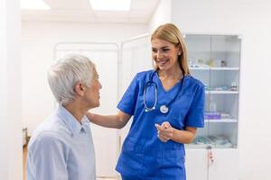 Doctor giving hope. Close up shot of young female physician leaning forward to smiling elderly lady patient holding her hand in palms. Woman caretaker in white coat supporting encouraging old person photo