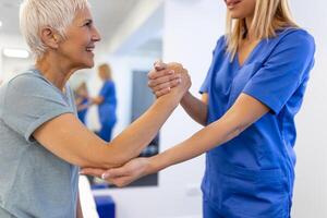 Caregiver helping contented senior woman exercise at clinic. Rehab for elder, senior medical care. Elder woman returning to good state of health photo