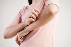 A woman with a pink shirt is scratching her arm photo