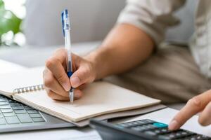 un hombre es escritura en un cuaderno con un bolígrafo y un calculadora foto