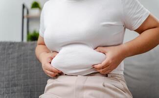 A woman is sitting on a couch and holding her stomach photo